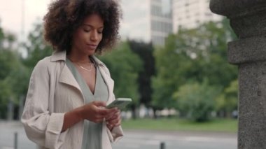 Şık kıyafetler ve aksesuarlarla güzel bir kadın akıllı telefonlara bakarken samimi bir şekilde gülümsüyor. Sokakta yürürken cep telefonu kullanan güzel Afrikalı Amerikalı kadın..