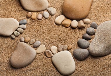 Trace feet of a pebble stone on the sea sand backdrop
