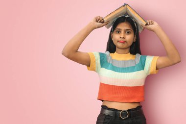 Şaşırmış, kararsız, kuşkucu, Hintli tatlı kız izole edilmiş bir kitabı kafasına koymuş ve fotokopi aletiyle doğrudan kameraya bakıyor..