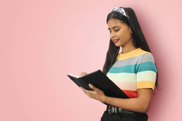 Gülümseyen Hintli Asyalı kız öğrenci yan yana poz veriyor. Kalemle not defterine notlar yazıyor. Not defterine doğru bakıyor..