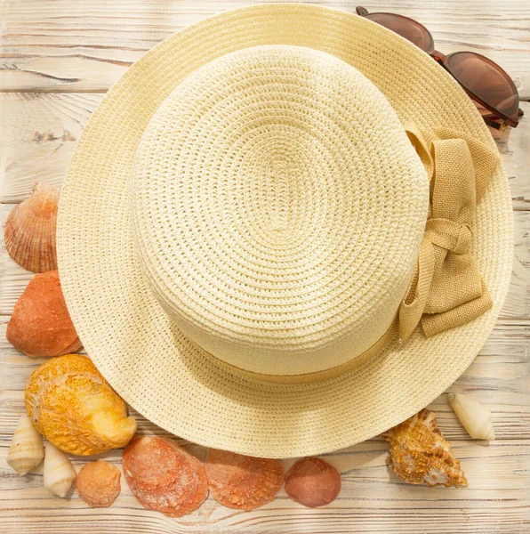 Beige hat and sun protection glasses. Summertime concept. Wattled head wear and natural shells on the wooden background.