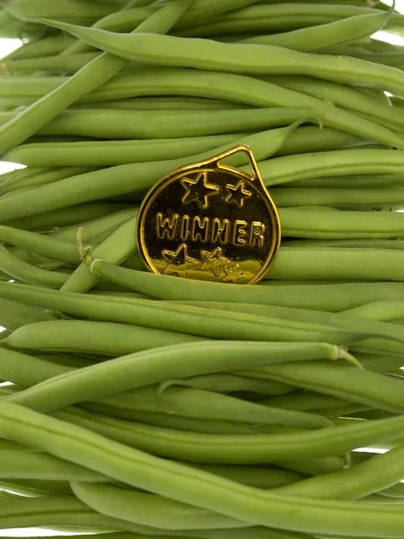 Green beans with a gold medal winner pendant on a wooden background — Stock Photo, Image