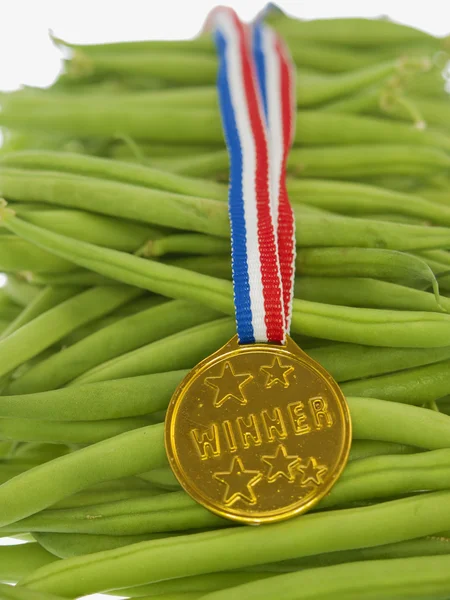 Feijão verde com um pingente vencedor da medalha de ouro em um fundo de madeira — Fotografia de Stock