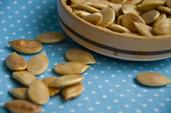 Dried pumpkin seeds in a brown artisan bowl on a blue napkin clo — Stock Photo, Image