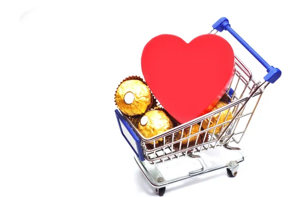 Valentine's day composition. Shopping cart full of chocolate candy and big red heart isolated on white — Stock Photo, Image
