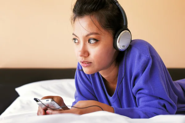 Jovem mulher em fones de ouvido ouvindo a música na cama — Fotografia de Stock