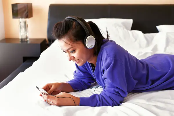 Ung kvinna i hörlurar lyssna på musik i sängen — Stockfoto