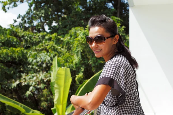 Mujer joven en un sombrero y gafas de sol de pie en un balcón —  Fotos de Stock