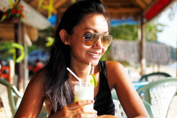 Junge Frau in schwarzem Top und Sonnenbrille bei einem Drink in einem Strandrestaurant in Thailand an einem sonnigen Sommertag — Stockfoto