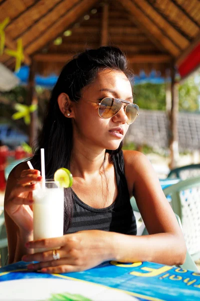 Mujer joven en un top negro y gafas de sol disfrutando de una bebida en un restaurante de playa en Tailandia en un día soleado de verano —  Fotos de Stock