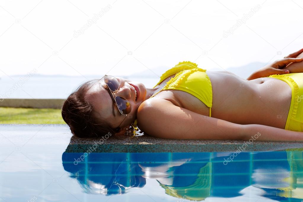Young woman in yellow swimsuit laying down next to swimming pool