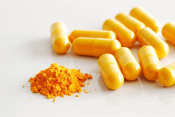 Une poignée de capsules de curcuma avec le contenu d'un déversement — Photo