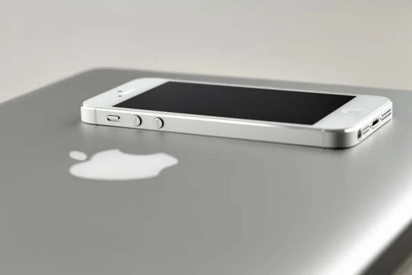 Ένα λευκό iphone 5 τοποθέτηση ένα κλειστό καπάκι της ένα apple macbook pro lap-top — Φωτογραφία Αρχείου