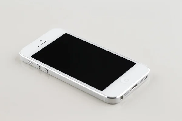 Een gloednieuwe witte smartphone op een witte reflecterende achtergrond — Stockfoto
