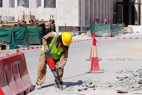 Um trabalhador usa um martelo pneumático para quebrar um pavimento de concreto — Fotografia de Stock