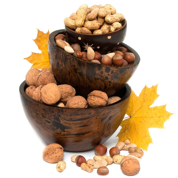 Орехи в деревянной чаше с желтыми листьями клена на белом фоне — стоковое фото