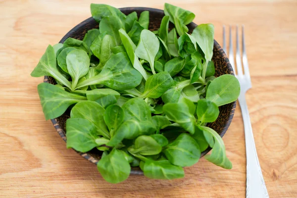 Wooden bowl with corn salad leaves — Stock Photo, Image