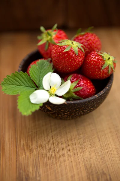 Fresas frescas en un tazón de madera sobre un fondo de madera — Foto de Stock