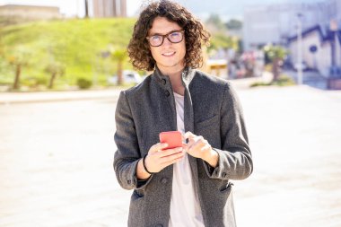 Uzun saçlı adam yürüyor ve akıllı bir telefon kullanıyor.