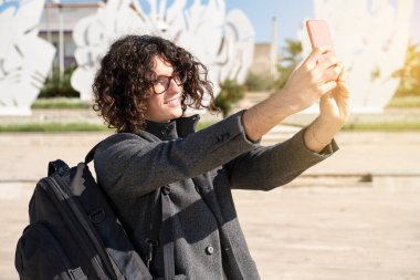 Yakışıklı genç adam sokakta selfie çekiyor.
