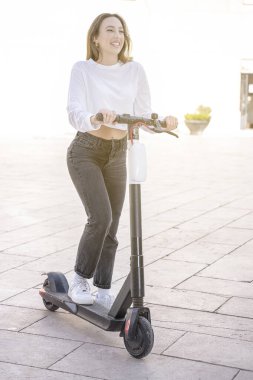Mutlu gülümseyen bir kadının güneşli bir günde scooter sürerken çekilmiş dikey fotoğrafı.