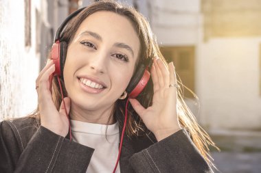Milenyum kadınının portresi. Kulaklıkla müzik dinliyor. Şehirde gülümsüyor.
