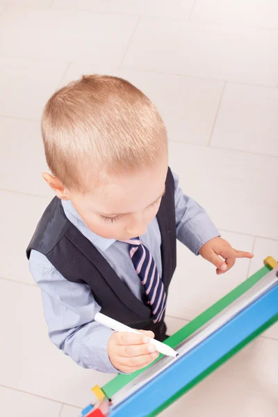 Traje de niño pequeño trabajando en la pizarra —  Fotos de Stock