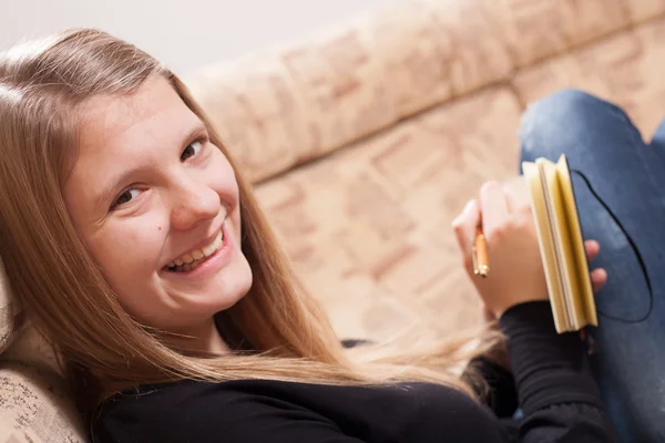 Glücklicher Teenager, der im Wohnzimmer auf dem Sofa sitzt und Tagebuch schreibt — Stockfoto