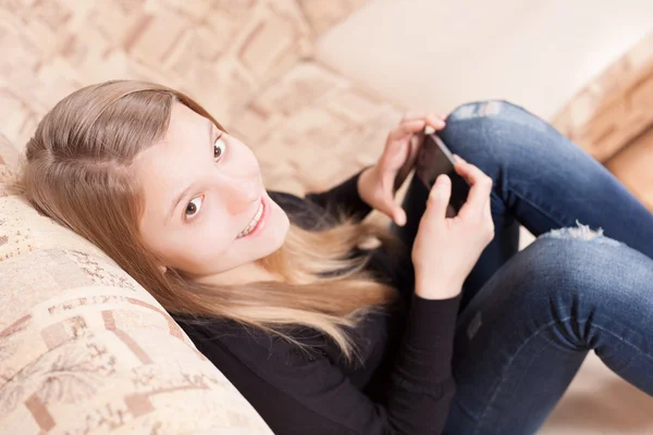 Boldog teen mobiltelefon ül a díványon, a nappaliban — Stock Fotó