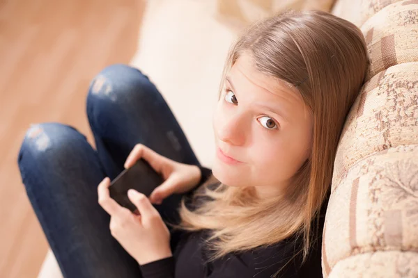 Adolescente felice con cellulare seduto sul divano in soggiorno — Foto Stock