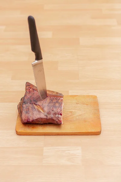 Carne fumada caseira em tábua de corte de madeira com faca grande Fotografia De Stock