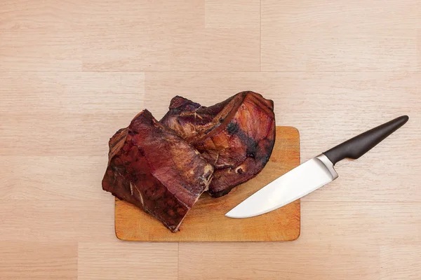 Carne fumada caseira em tábua de corte de madeira com faca grande Imagem De Stock