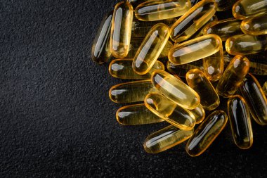Siyah zemin üzerinde Omega-3 kapsülleri yığını.