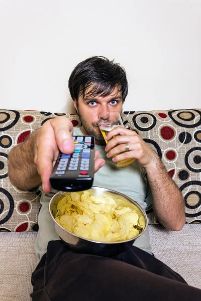 Jovem assistindo televisão, comendo batatas fritas e bebendo — Fotografia de Stock