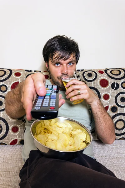 Joven viendo televisión, comiendo papas fritas y bebiendo —  Fotos de Stock