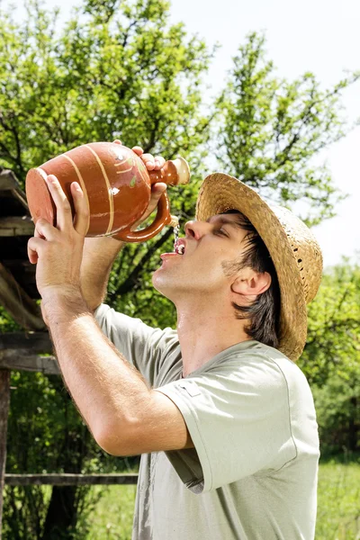 Жаждущий молодой человек в соломенной шляпе пьет воду из керамического j — стоковое фото