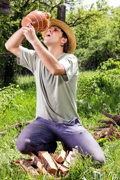 Thirsty young man with straw hat drinking water from a ceramic j — Stock Photo, Image