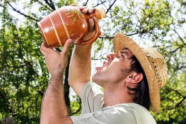 Жаждущий молодой человек в соломенной шляпе пьет воду из керамического j — стоковое фото
