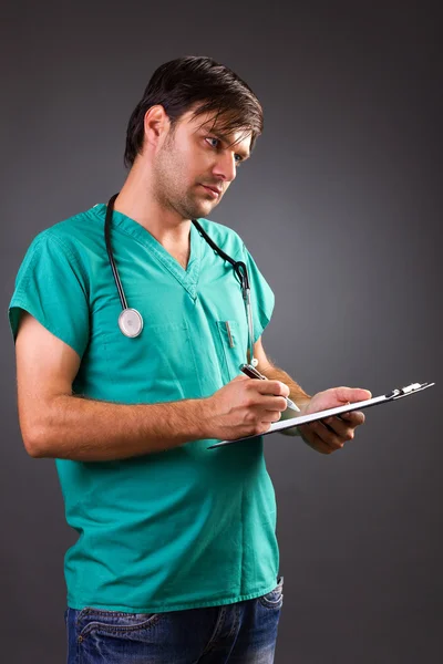 Young doctor with stethoscope writing on clipboard — Stock Photo, Image