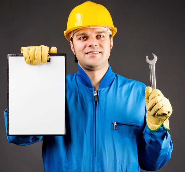 Retrato de un joven trabajador sosteniendo un portapapeles en blanco y una llave inglesa — Foto de Stock