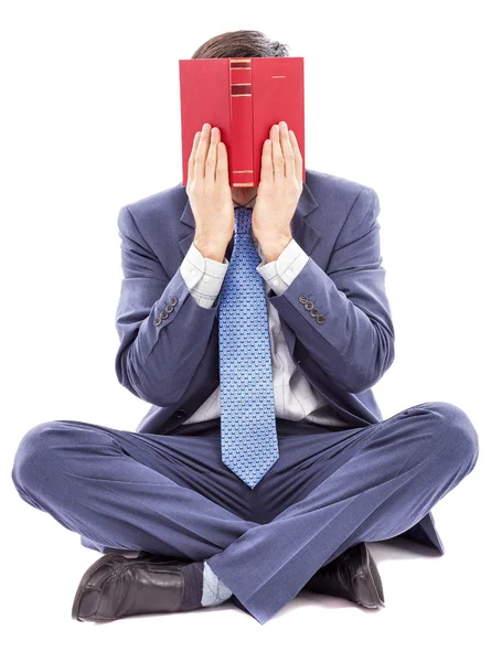 Geschäftsmann sitzt im Schneidersitz und verdeckt sein Gesicht mit einem Buch — Stockfoto