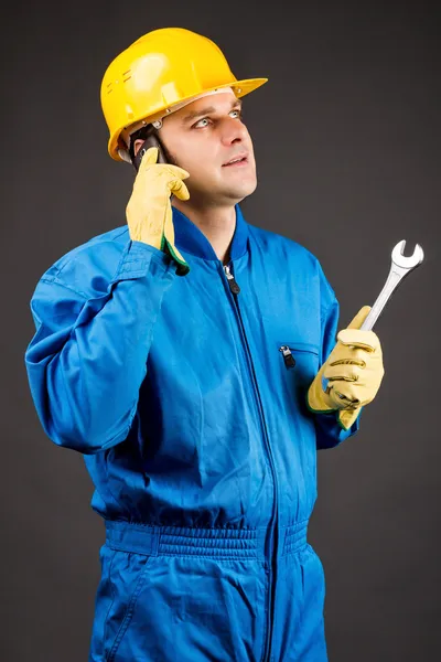 Junger Bauarbeiter telefoniert und hält Schraubenschlüssel in der Hand — Stockfoto