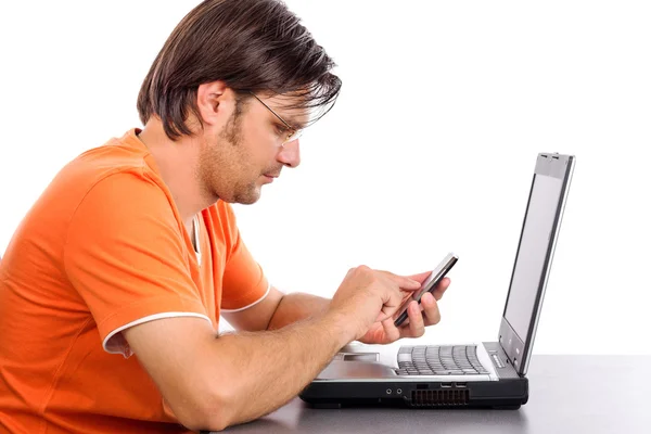 Young man using his smart phone while sitting in front of a lapt — Stock Photo, Image