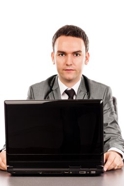 Genç işadamı ofis masasında oturuyor ve kameraya bakıyor.