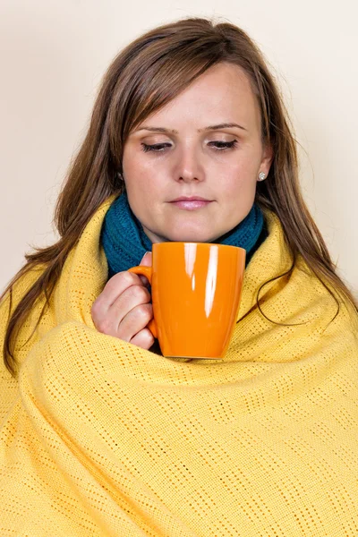 Mujer joven cubierta con una manta, sosteniendo una taza de té, sittin — Foto de Stock