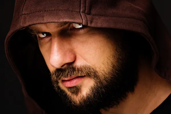 Close-up portrait of threatening man with beard wearing a hood — Stock Photo, Image