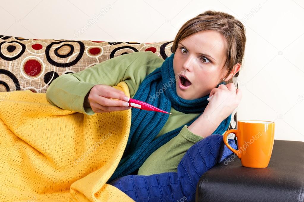 Expressive young woman having flu and checking thermometer