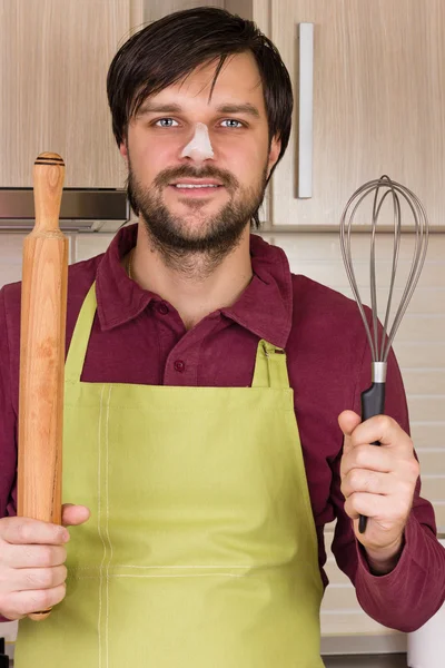 Smiling young man with apron holding a beater and a rolling pin — Stock Photo, Image