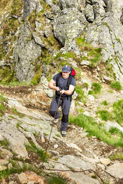 Man hiking on difficult mountain trail with hanging cable — Stock Photo, Image