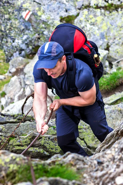 Młody człowiek piesze wycieczki na trudny górski szlakiem wisi kabel — Zdjęcie stockowe